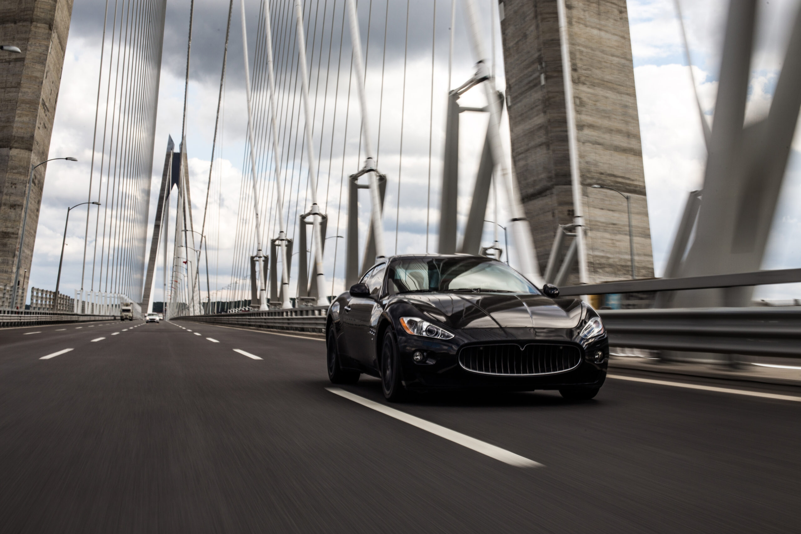 Black sedan driving across a suspension bridge